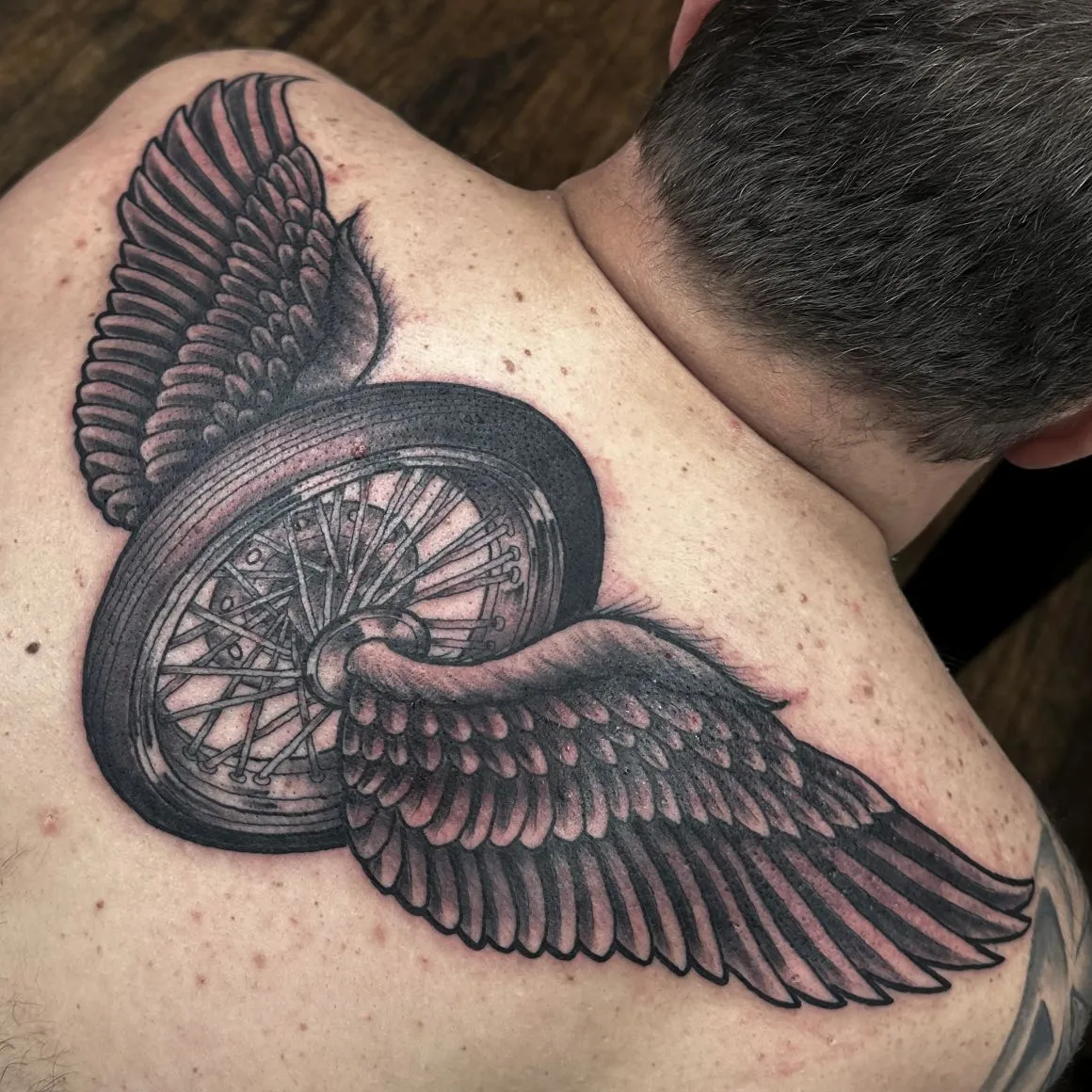 Black-and-grey winged wheel back tattoo